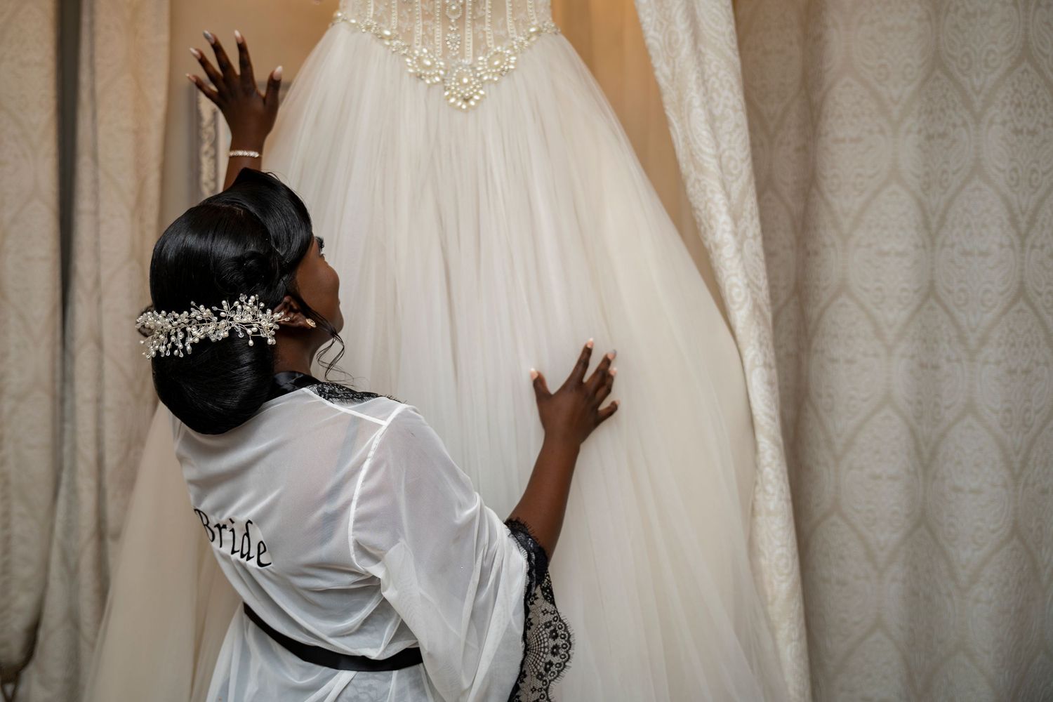 Bride in white robe touching her elegant ball gown wedding dress on a hanger.