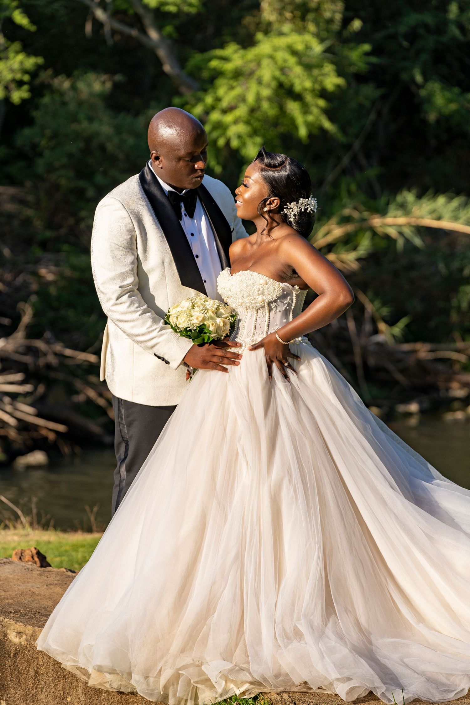 Bride and groom sharing a romantic moment outdoors near a river, bride in a strapless ballgown.