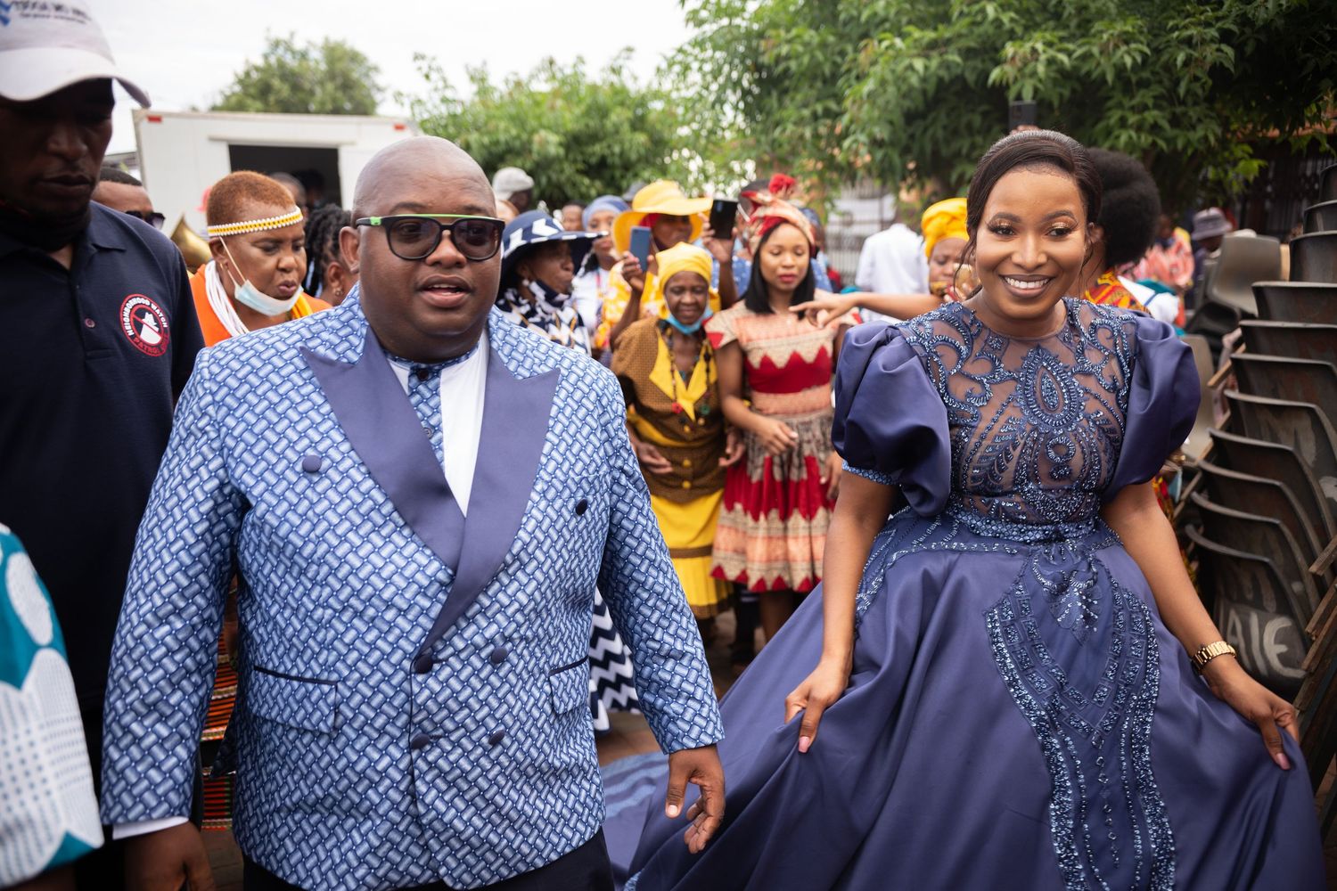 Couple in coordinating blue traditional African outfits walking together at a festive cultural ceremony.