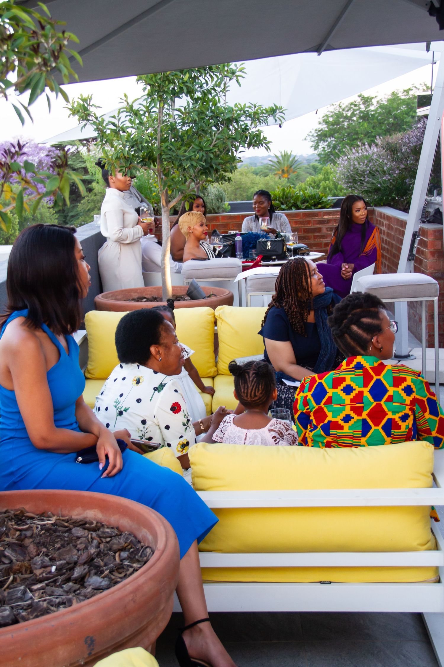 Guests relax on yellow outdoor sofas at a stylish rooftop social gathering.