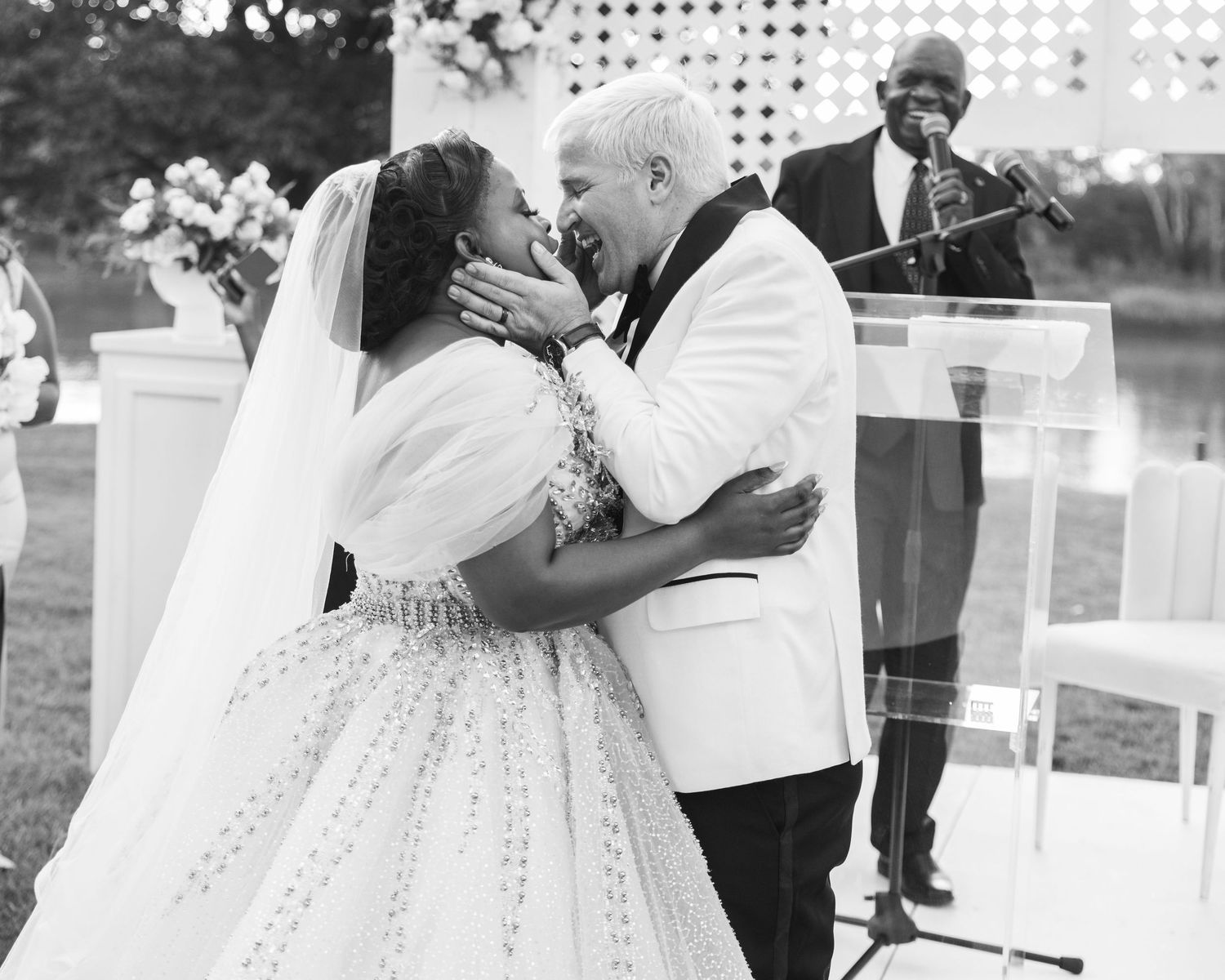 Black and white photo of a joyful couple sharing their first kiss at an outdoor wedding ceremony.