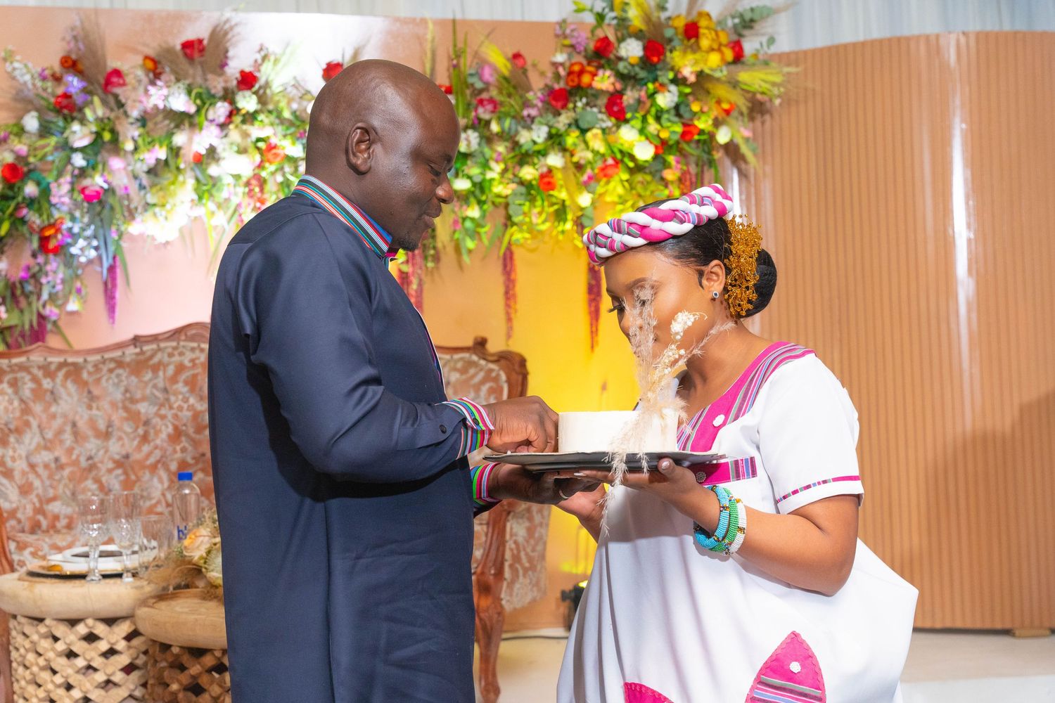 Couple exchanging gifts during a traditional African wedding ceremony with floral decorations in the background.