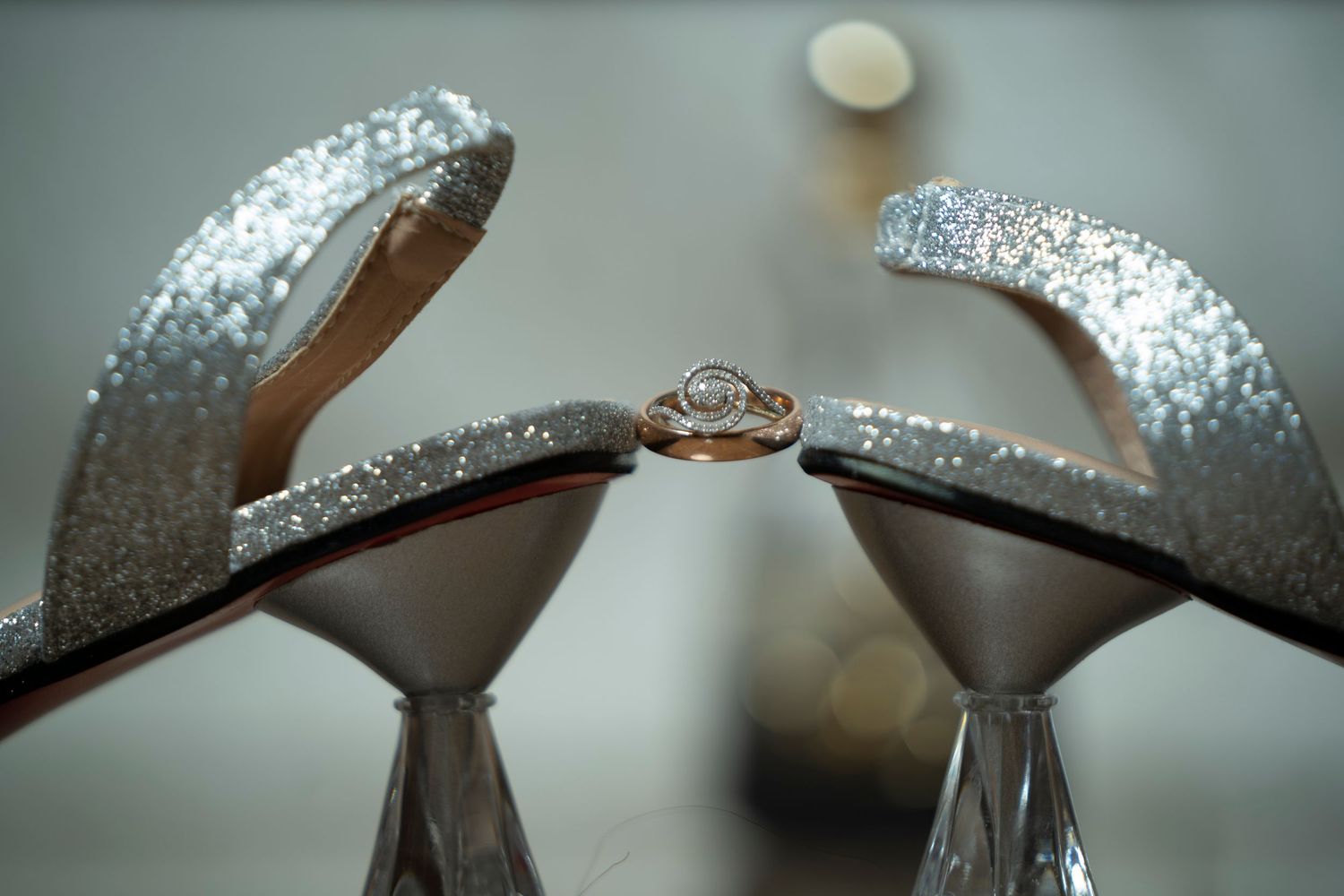 Diamond engagement ring displayed between pair of silver glitter high heel wedding shoes.