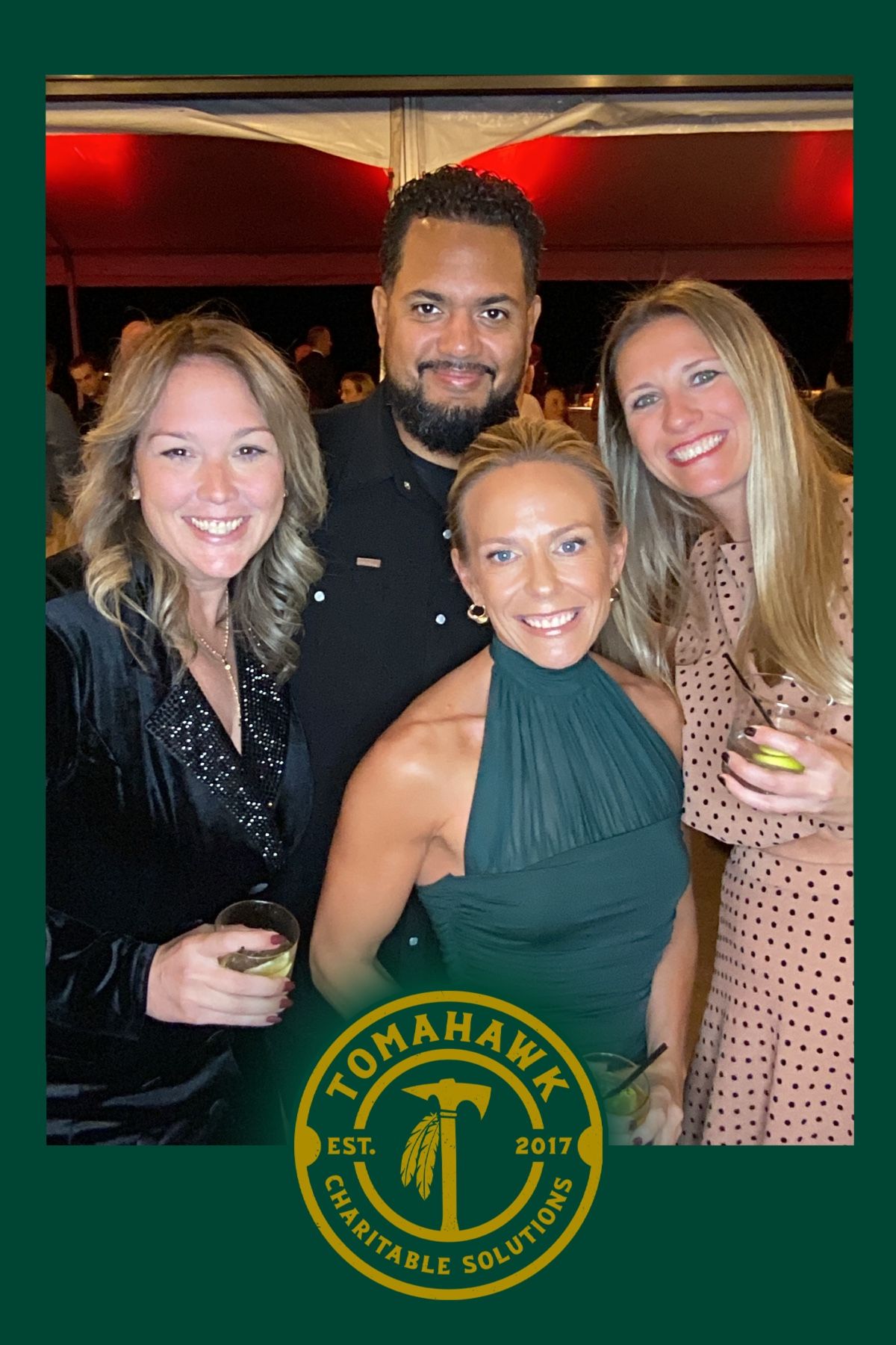 A group of friends smile together at an event with a green Tomahawk logo visible at the bottom of the photo frame.