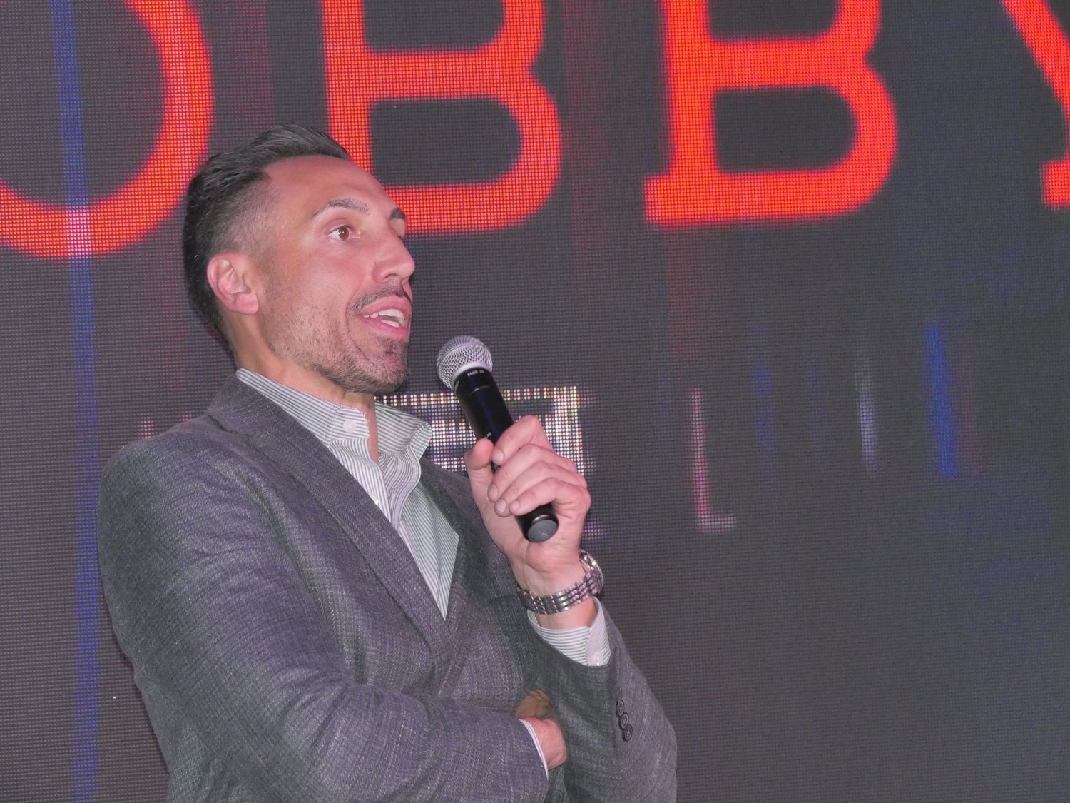 Speaker with animated expression holding microphone against red illuminated backdrop.