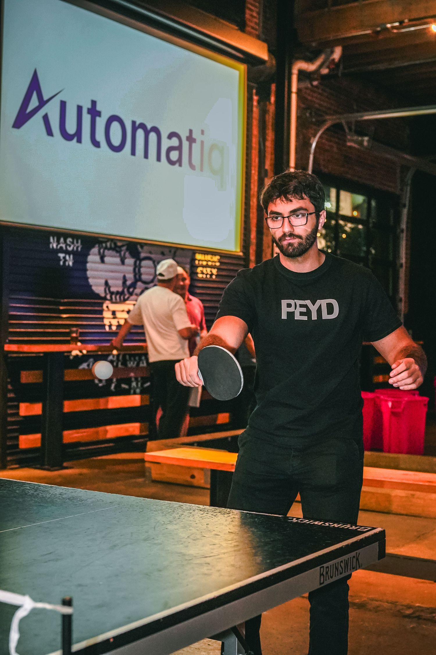 People playing ping pong at an indoor entertainment venue with branded signage.