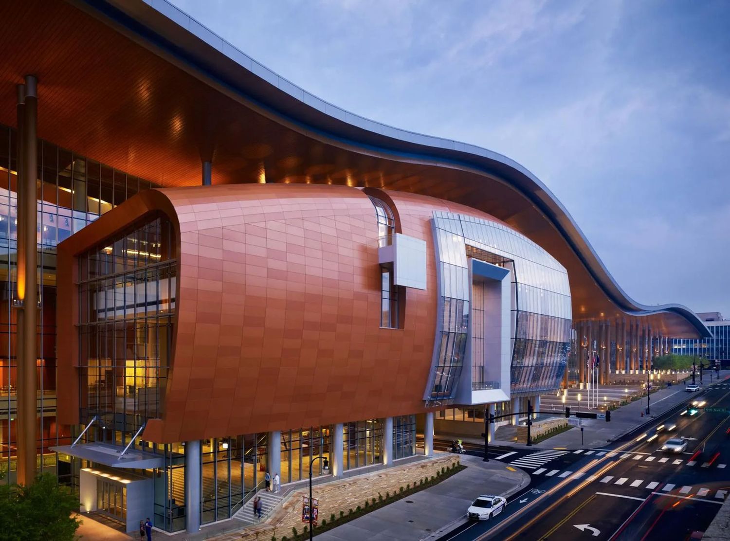 Modern curved architecture of a red-brown building with glass windows and walkways against a blue sky.