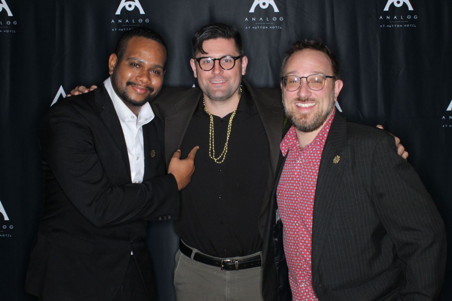 Group photo of people in formal attire at an event with black backdrop and logo.
