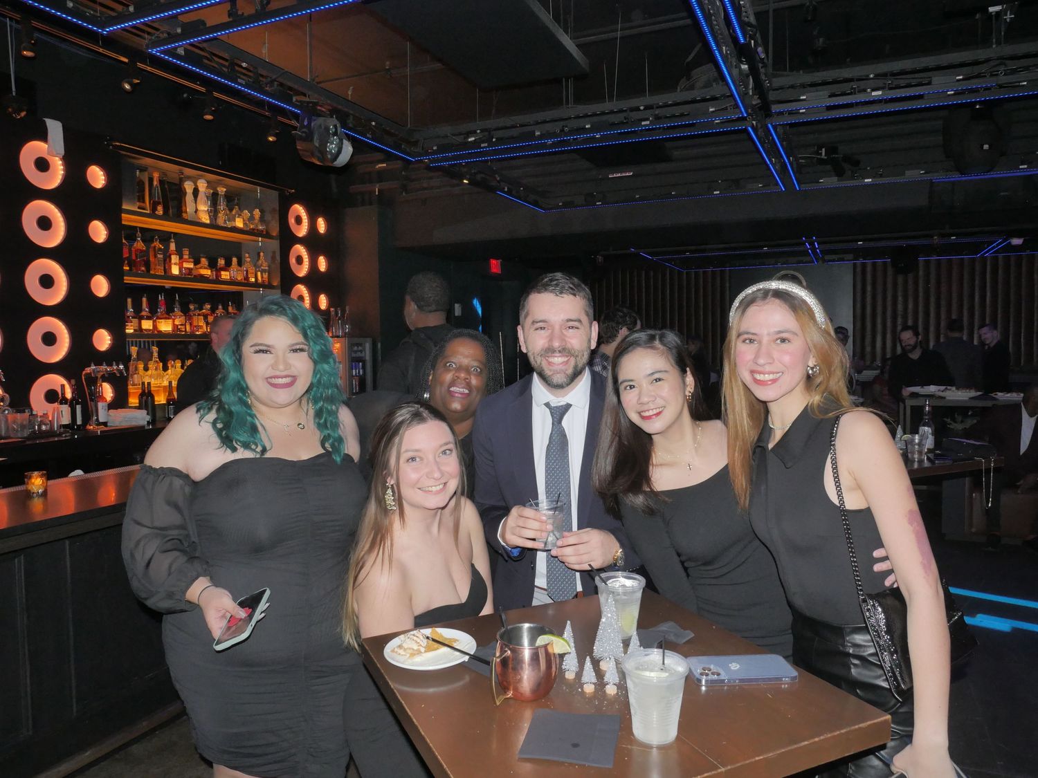 Group enjoying drinks and conversation at modern bar with neon lighting.