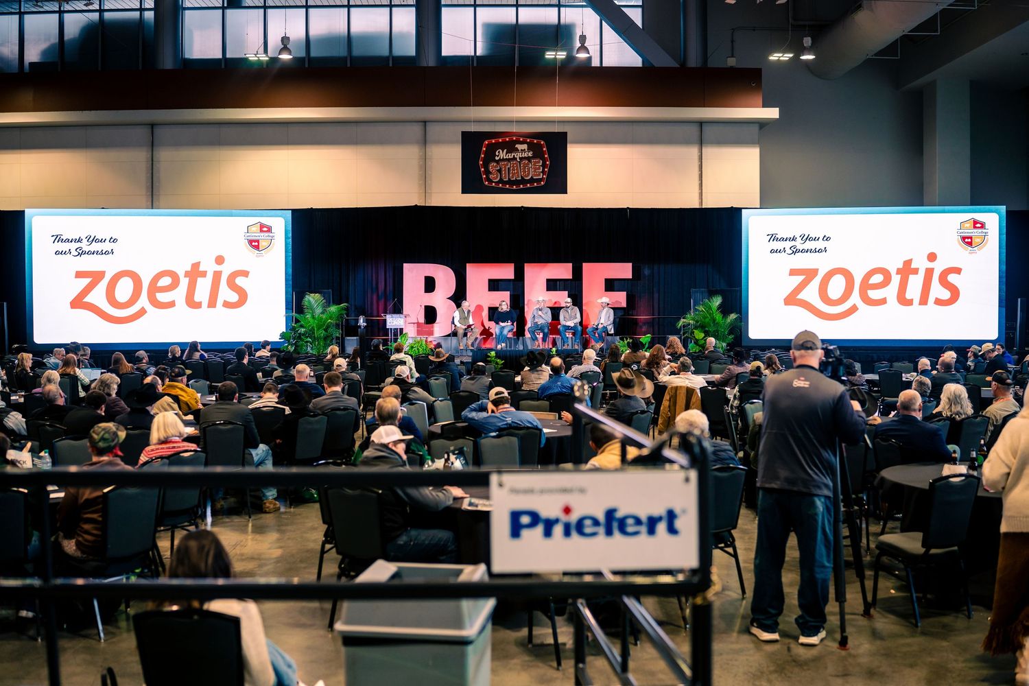 A busy indoor career fair with company booths and banners displaying logos for Zoetis and other organizations.