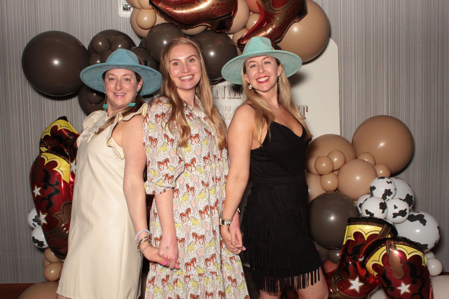 A group of friends pose together at a party with balloons and decorations visible in the background.