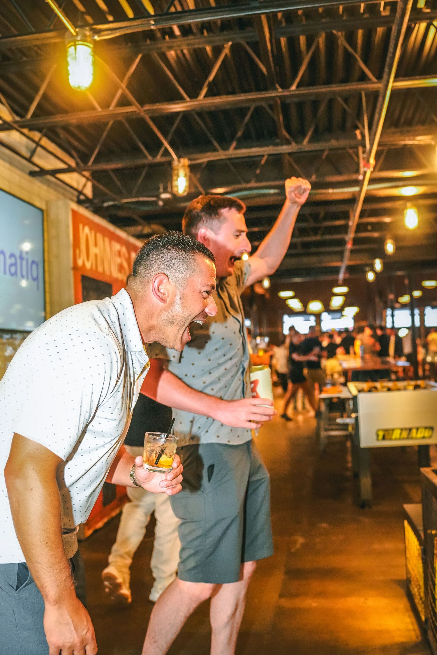 People having animated conversations in an industrial-style venue with warm lighting.