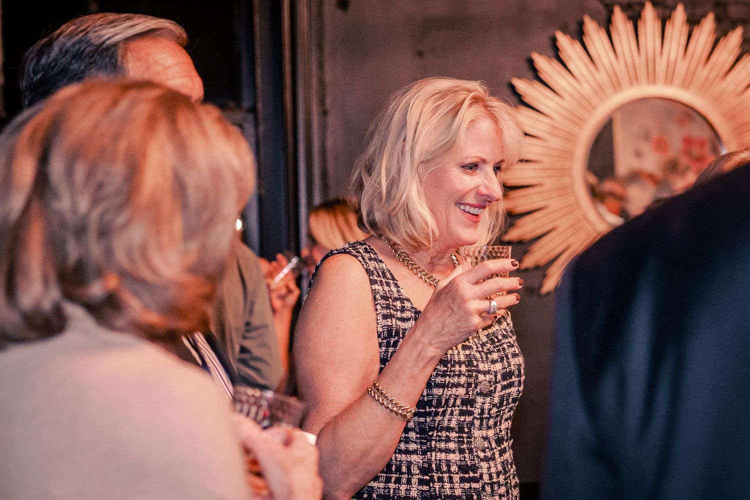 Partygoers laughing together with decorative sunburst art visible in background.