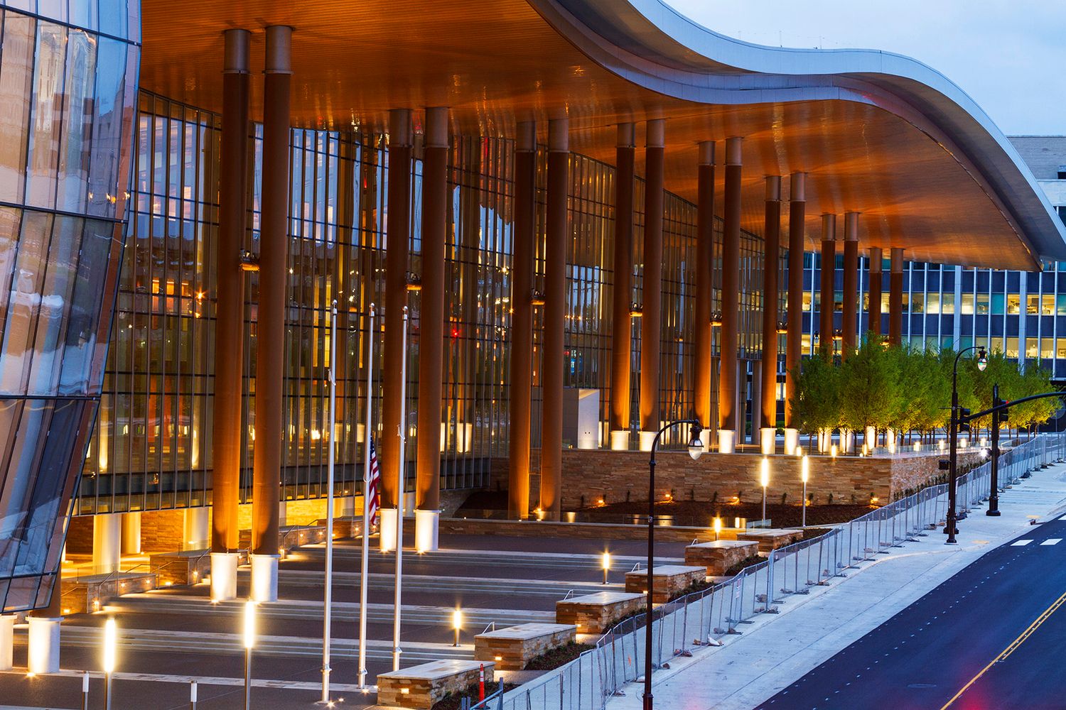 Modern glass building facade illuminated at dusk with curved architectural features and warm lighting reflections.