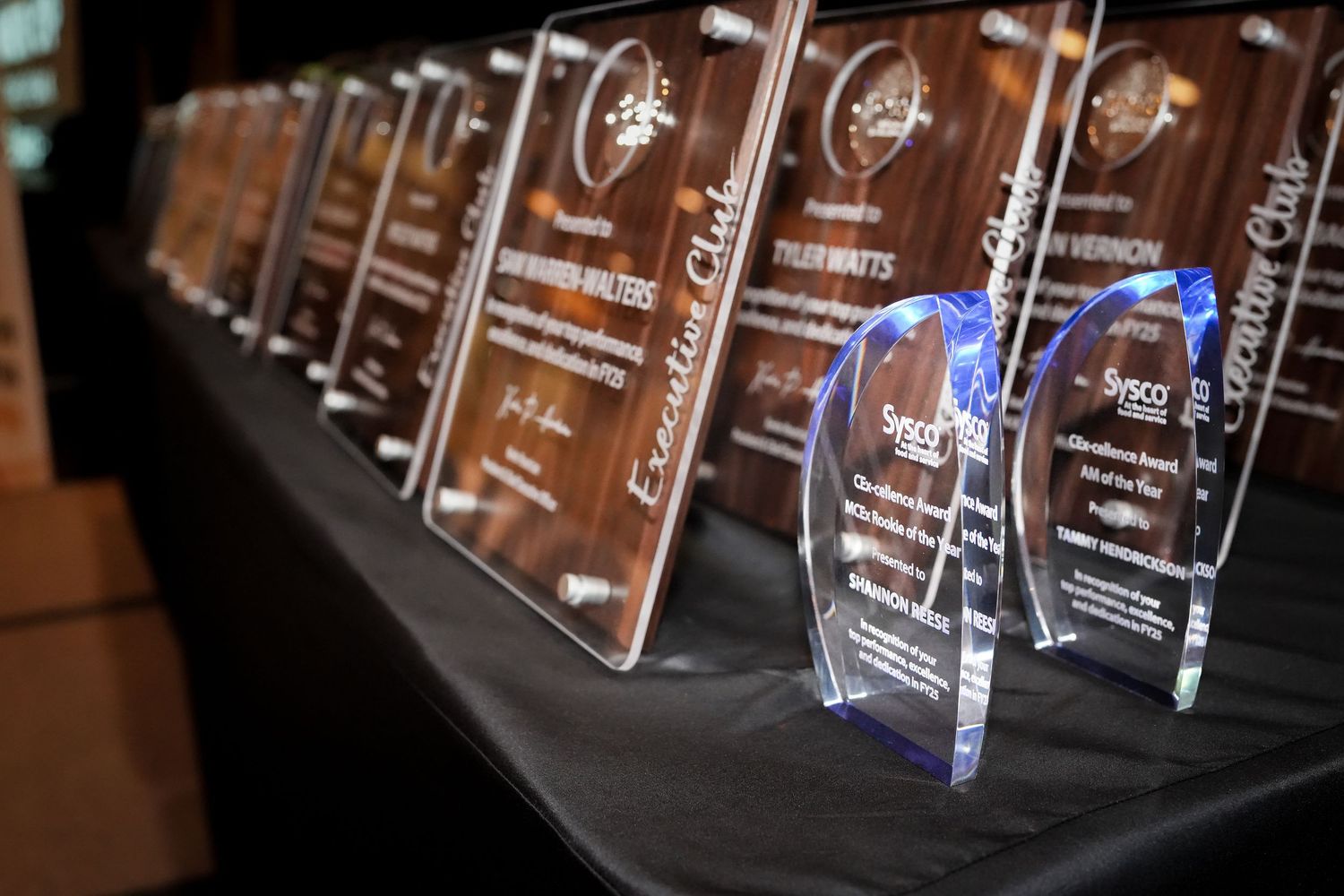 Row of illuminated crystal or glass awards displayed on a dark surface.