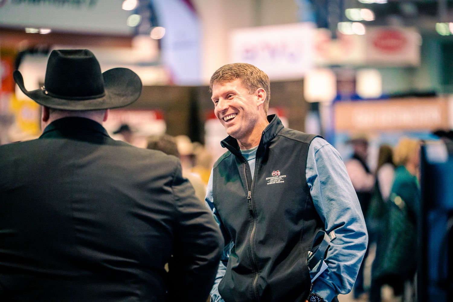 Two people in business attire share a friendly embrace during what appears to be a professional conference or event.