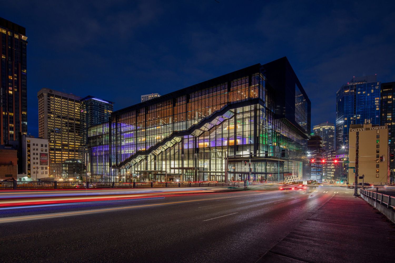 Modern glass convention center illuminated at night with light trails from passing cars on downtown Minneapolis street.