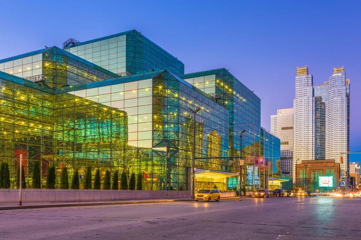 Modern glass office buildings with blue and green reflective facades illuminated at dusk in an urban setting.