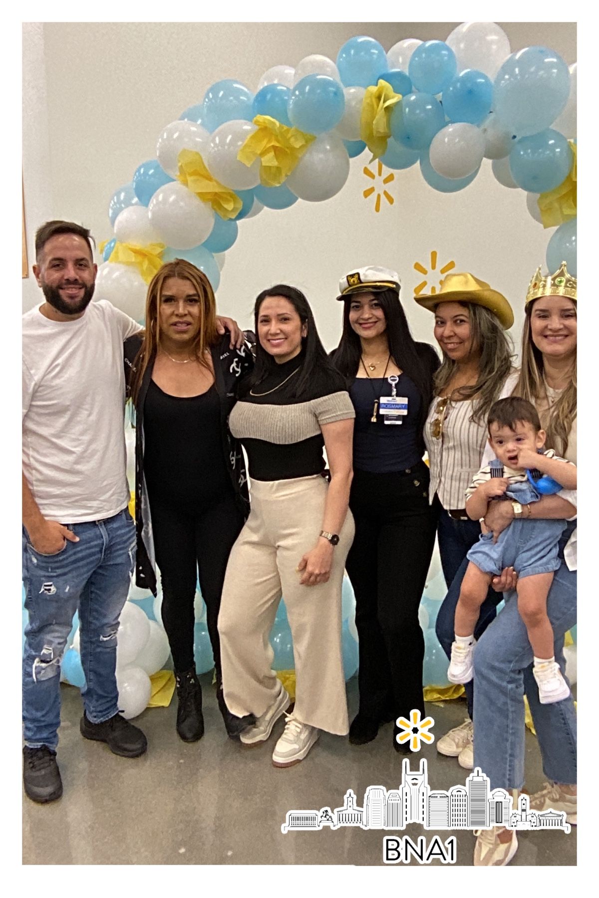 Group photo at a celebration event with blue and yellow balloon arch decorations in the background.