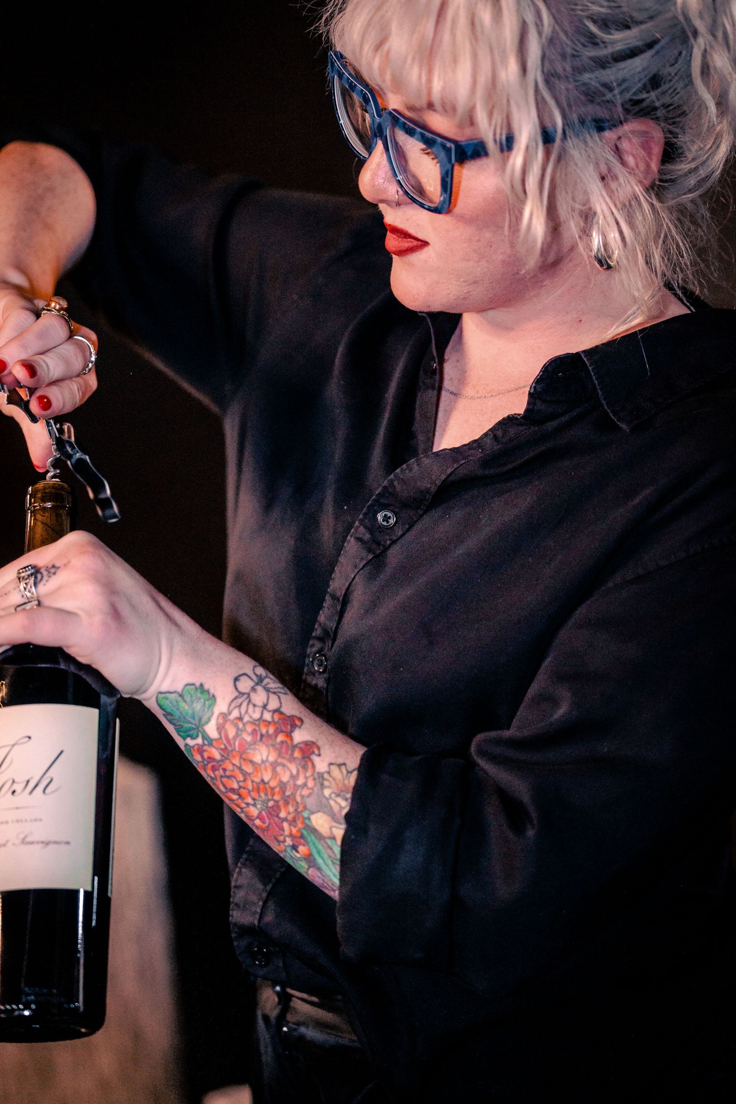 Close-up of wine bottles and glasses being served at a dark indoor venue.