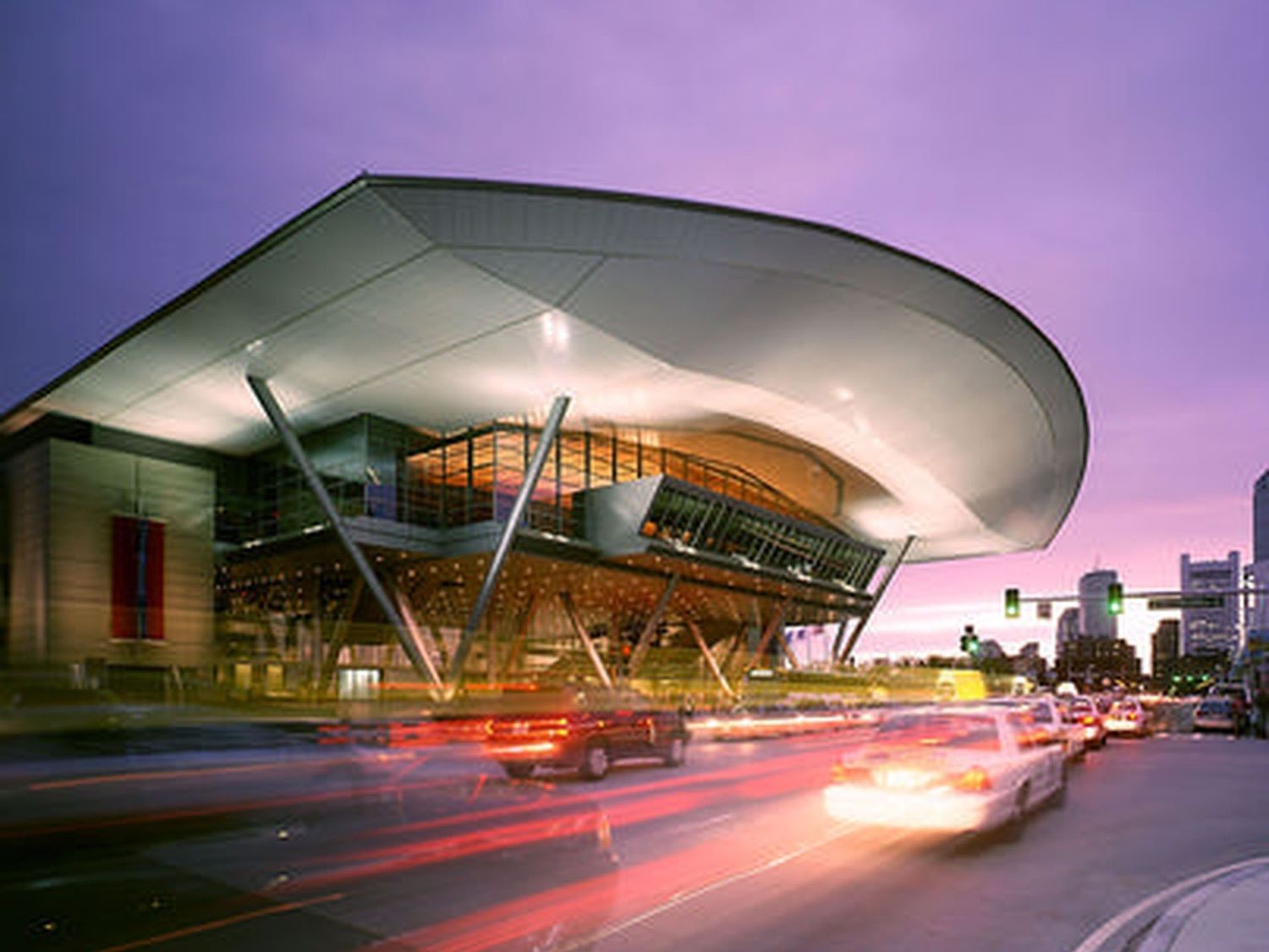 Modern airport terminal building exterior with streaking red light trails from passing vehicles at twilight.