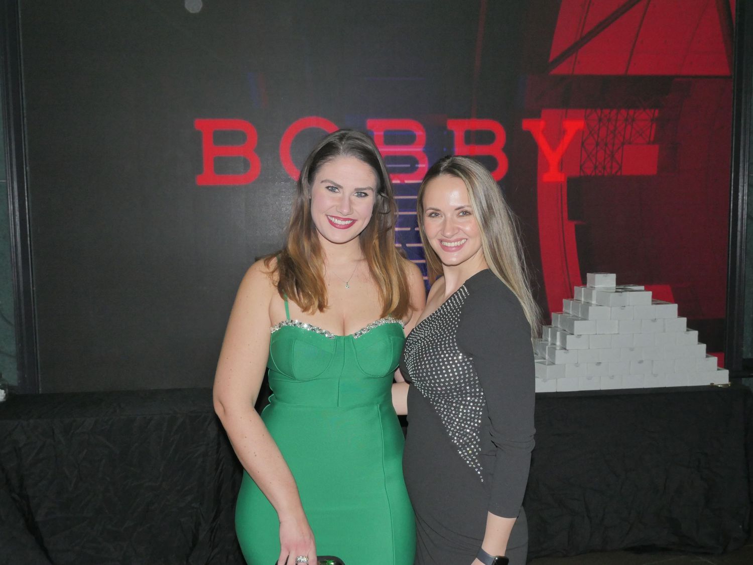 Friends posing together at a venue with red lighting and dark walls.