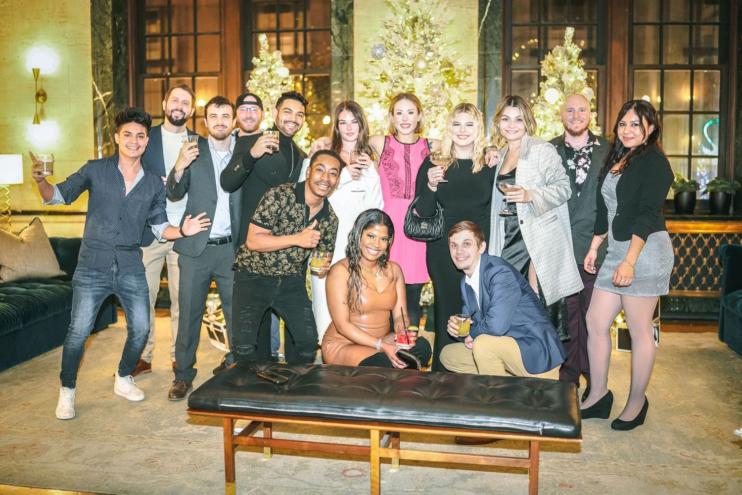 Large group photo of party guests gathered in front of a decorated Christmas tree.