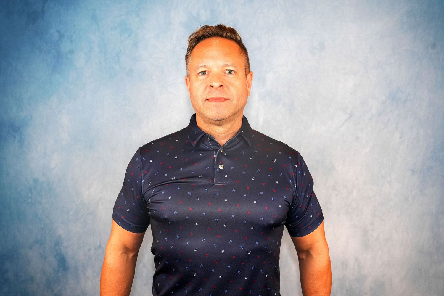 Professional headshot of person in dark polo shirt against blue background.