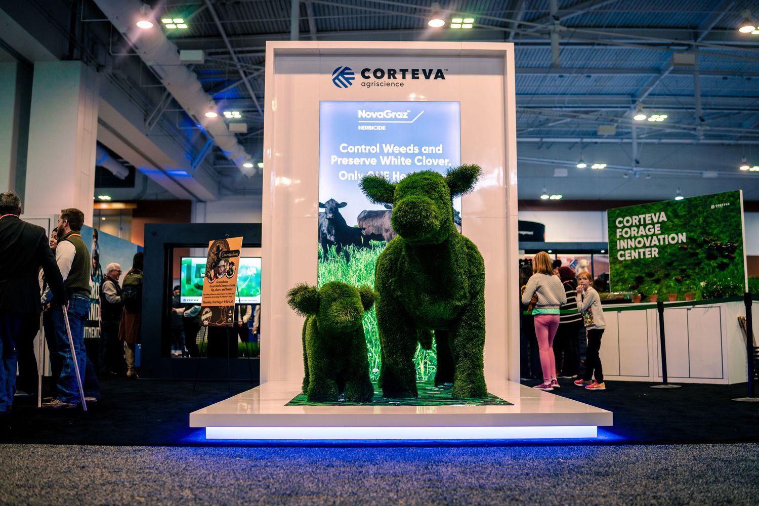 Green topiary bear sculptures on display at a trade show booth with white platform and lighting effects.