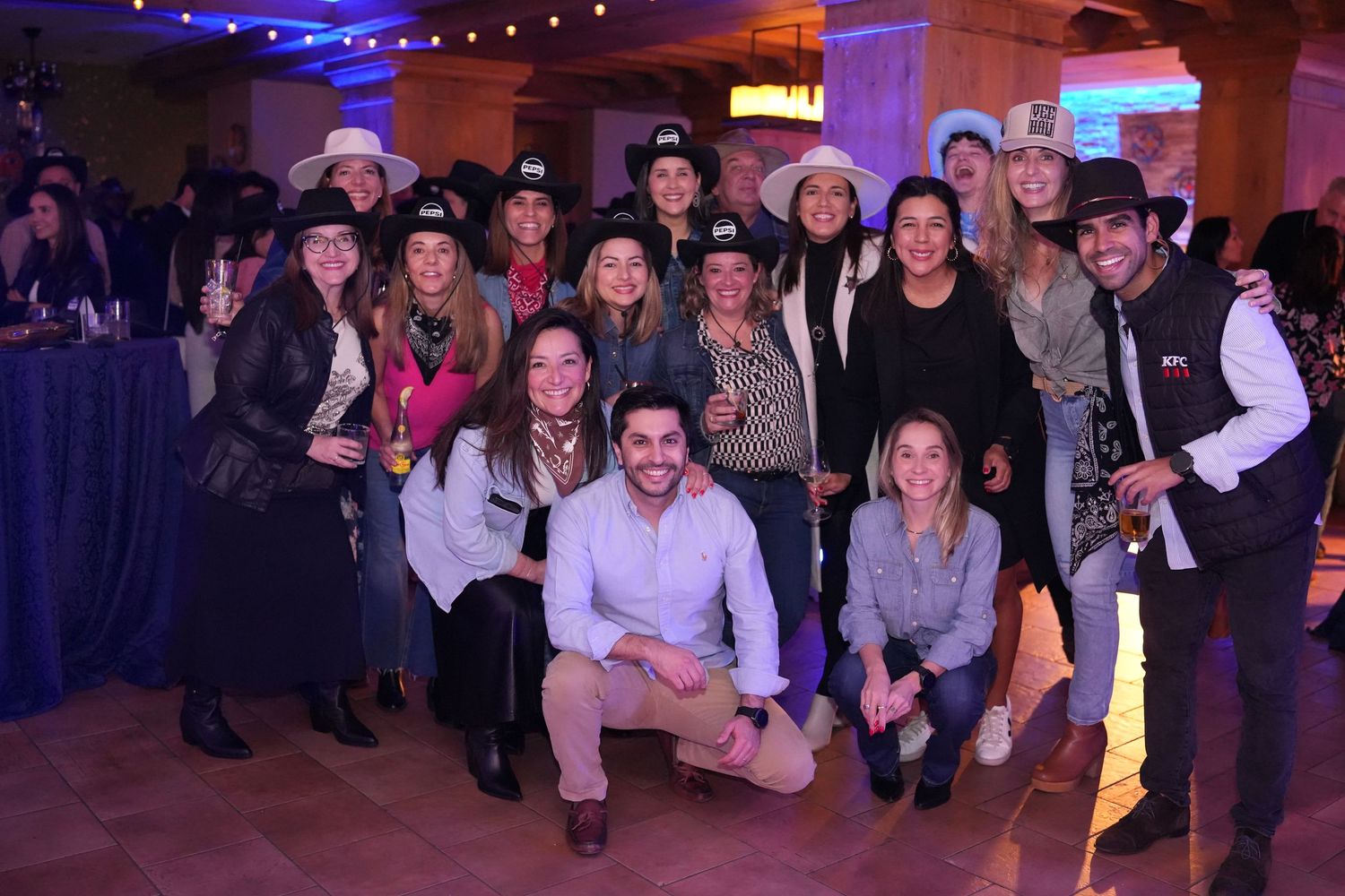 Large group photo of event attendees in western-themed attire at a party venue.