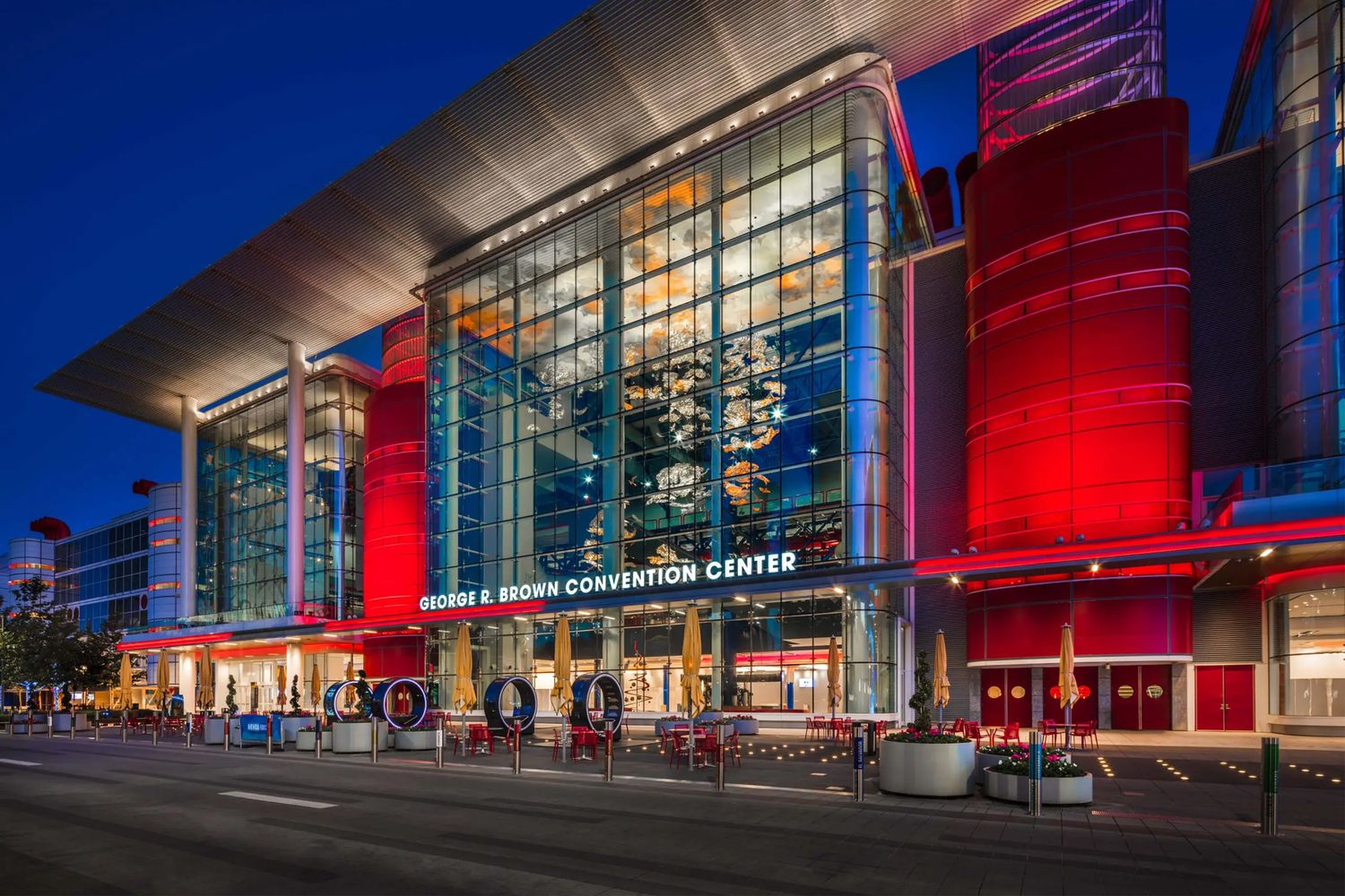 Modern convention center building exterior illuminated in vibrant red and blue lighting at night.