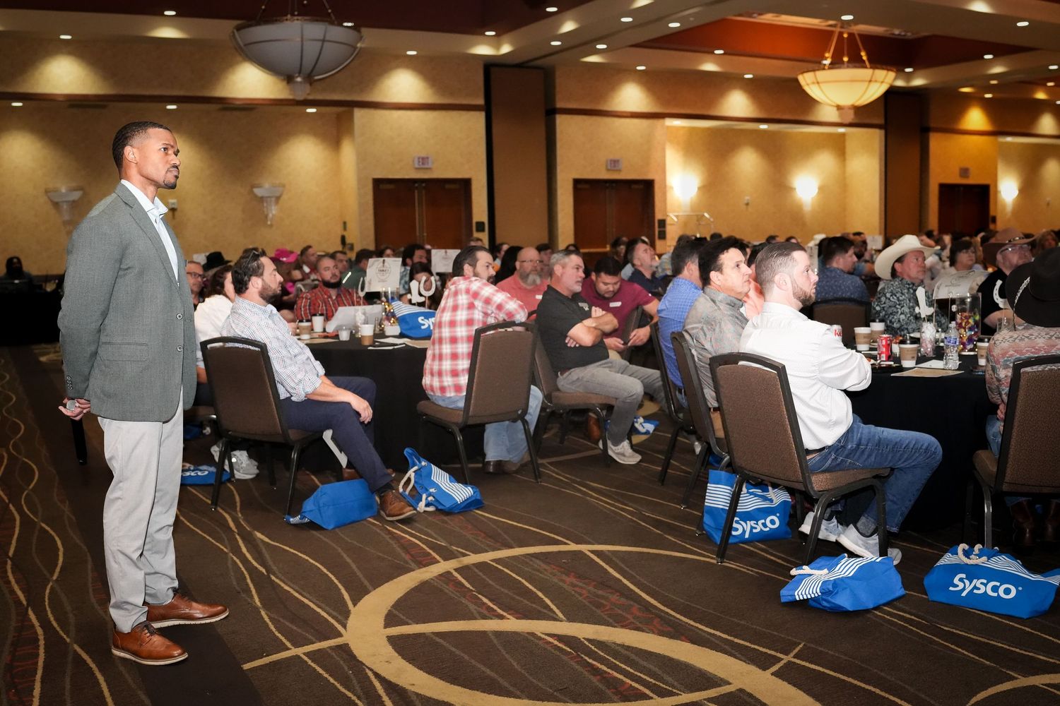 Large conference room filled with attendees seated at round tables.