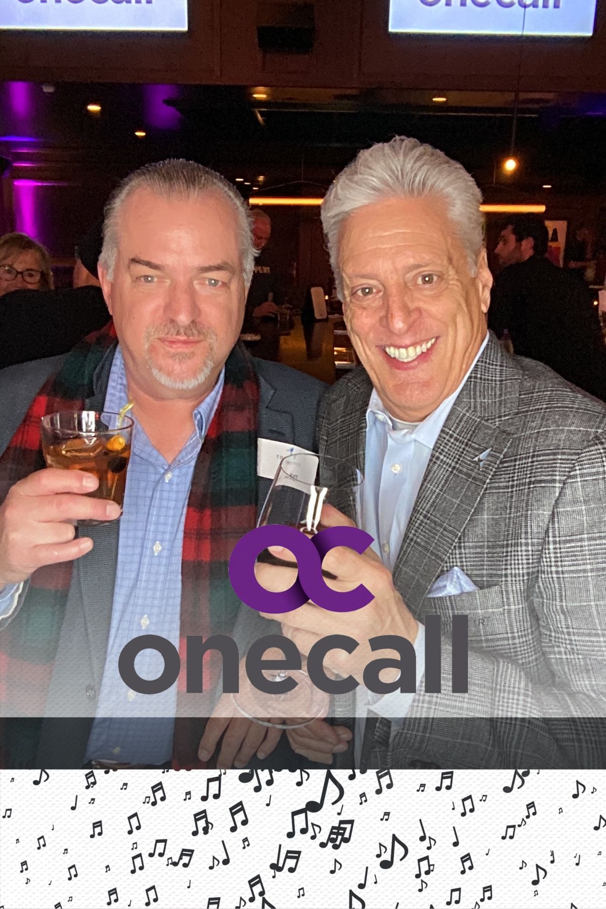 Two men in business attire smile together at a dimly lit venue with purple lighting in the background.
