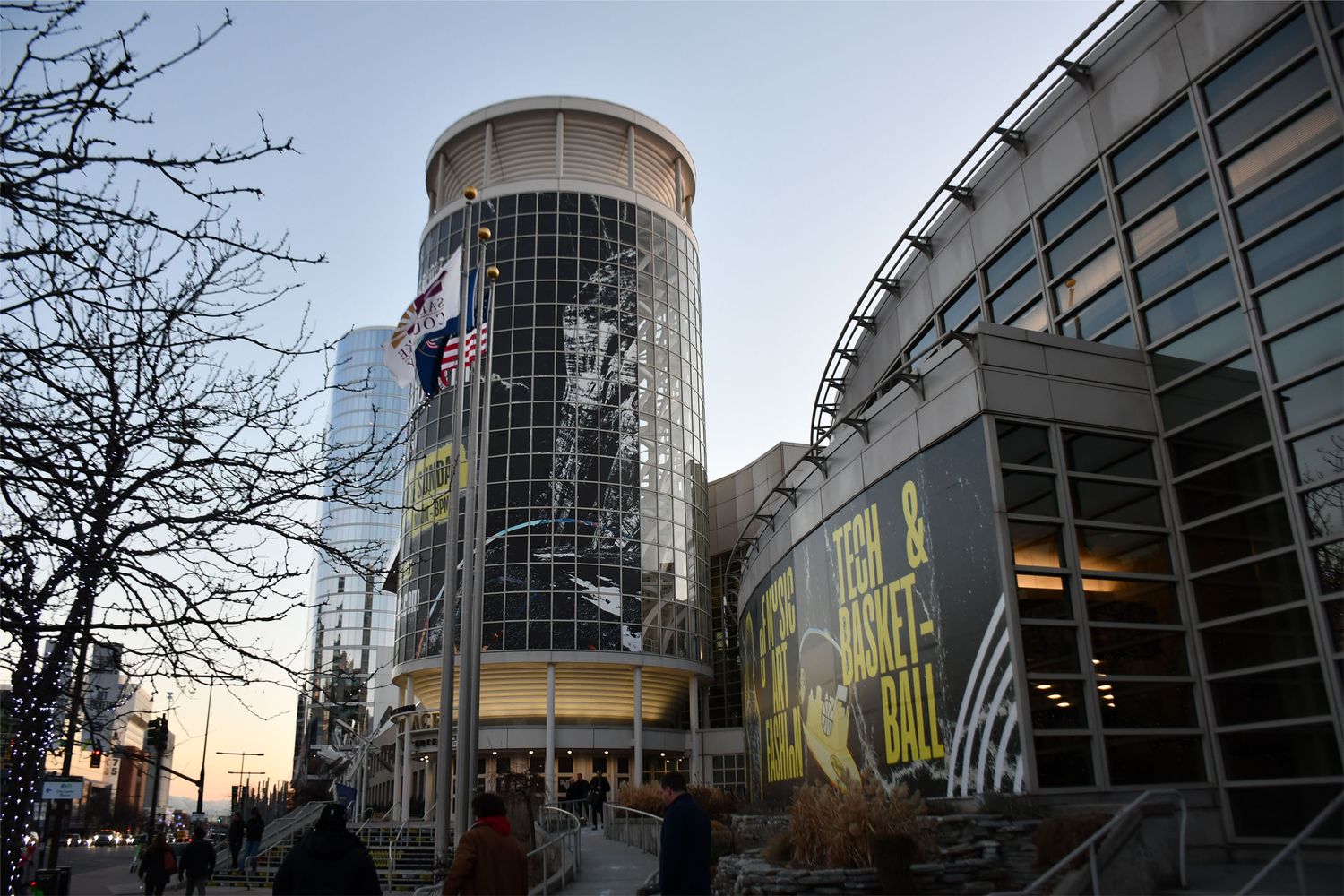 Modern glass office buildings with curved architecture photographed at dusk with bare tree branches visible.