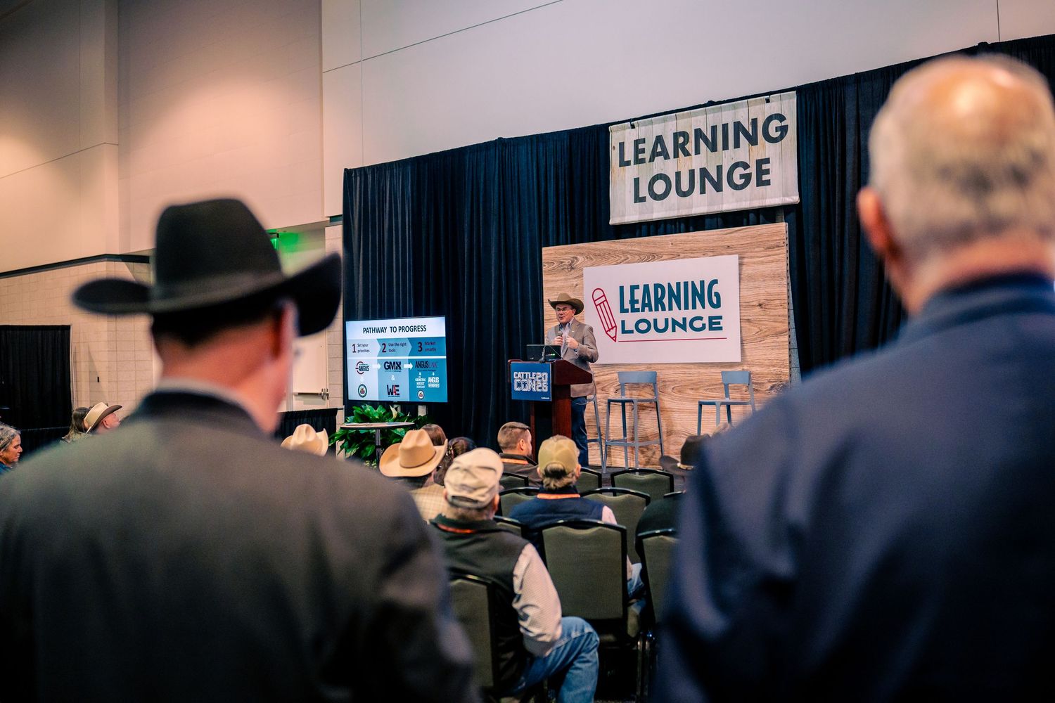 A group of people gather in a learning lounge area with signage and displays visible in the background.