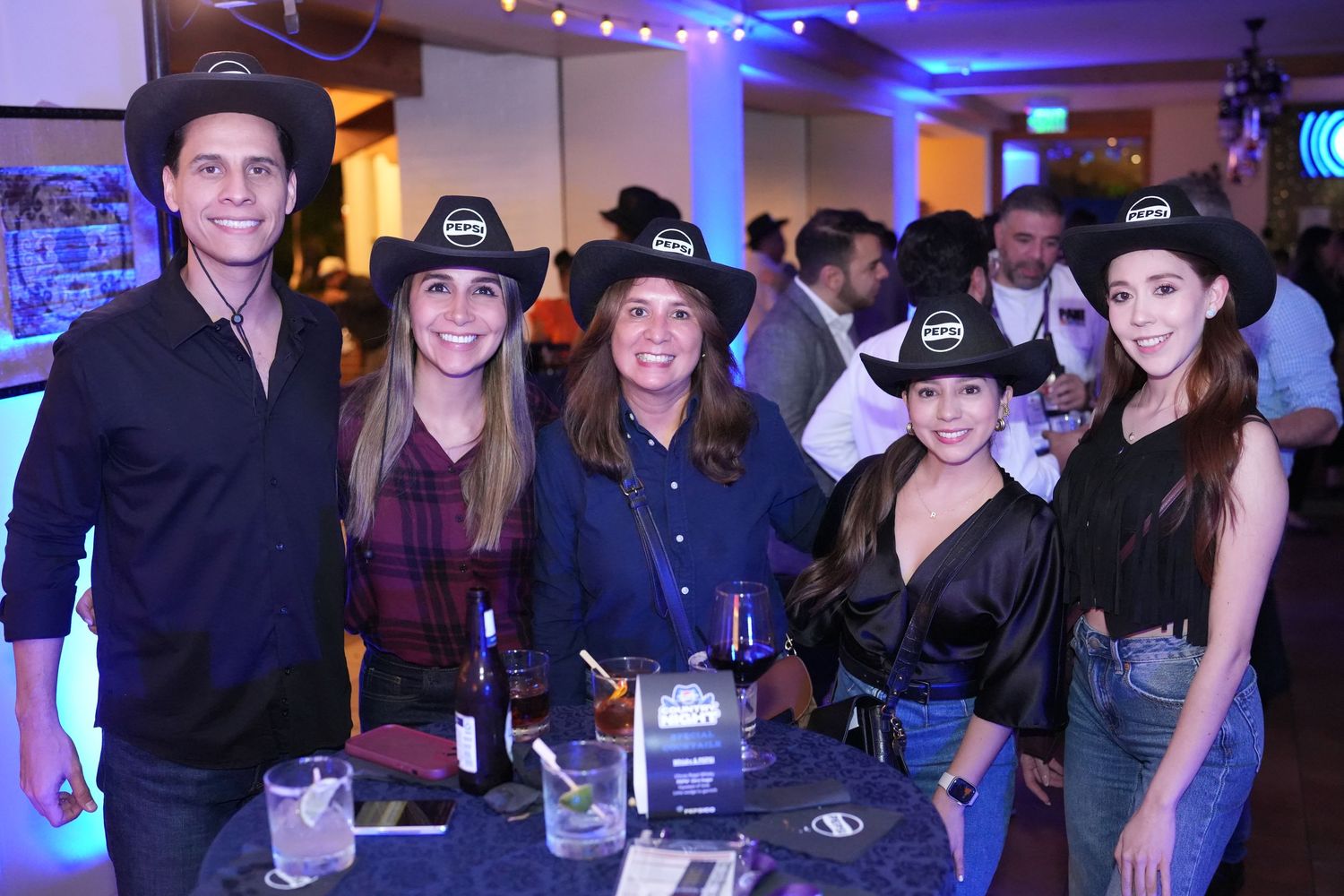 Party attendees in western wear gathered for group photos under blue ambient lighting.