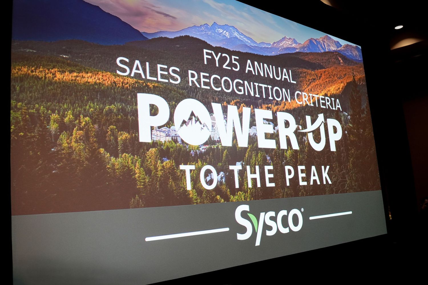 Scenic mountain landscape backdrop with corporate event text overlays and Sysco branding.