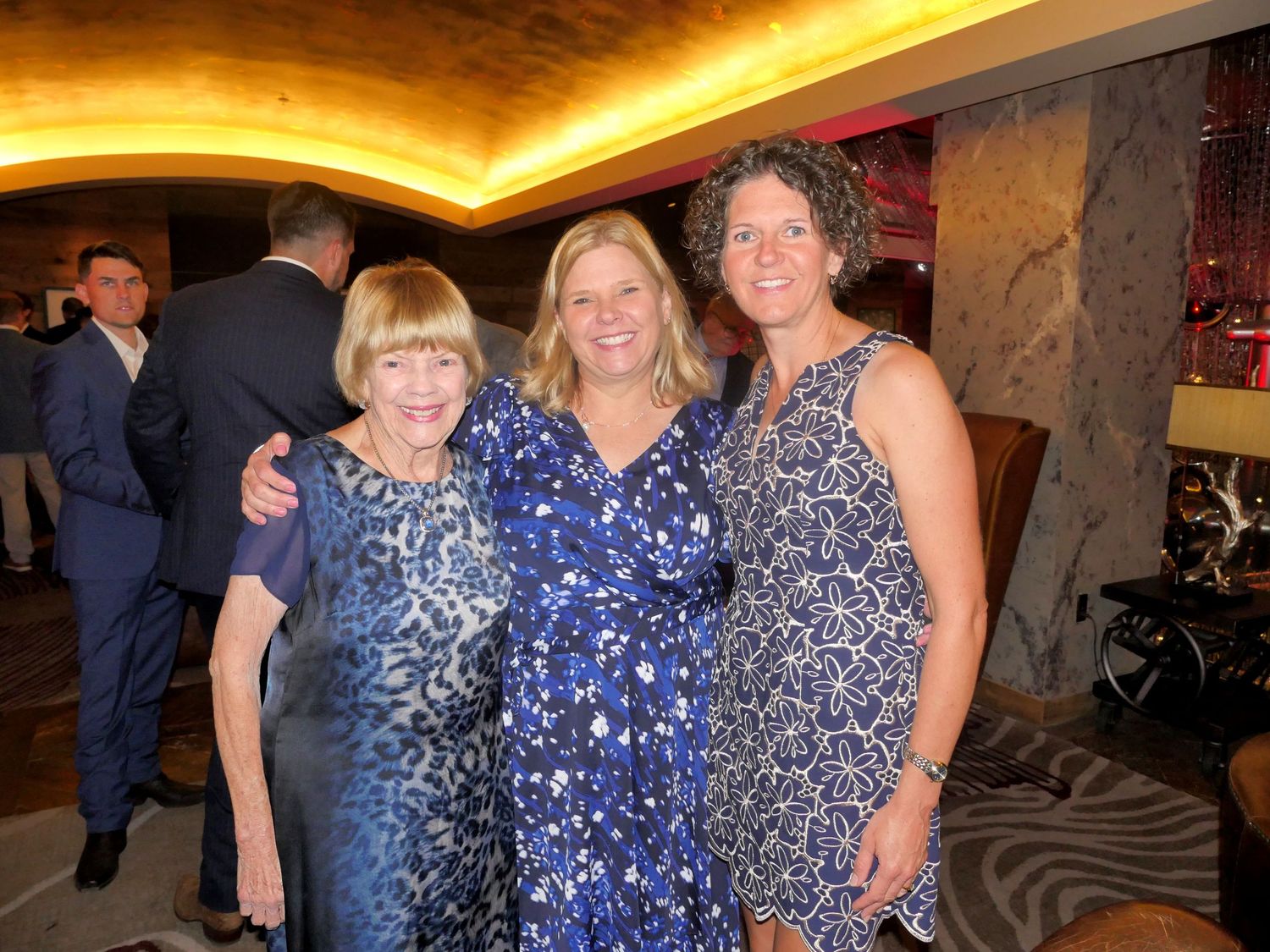 Three women in sparkly blue dresses posing together at formal event.