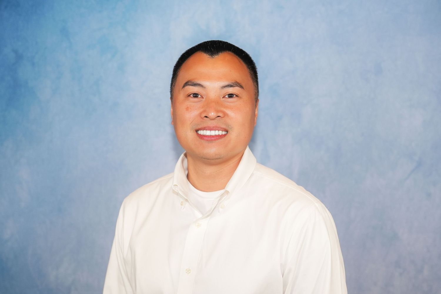 Professional headshot of person in white collared shirt against blue background.