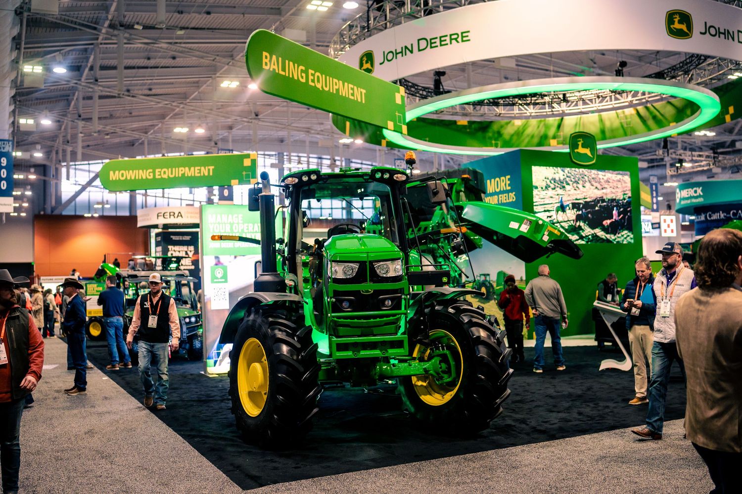 Green John Deere agricultural equipment and tractors on display at a large indoor farming machinery trade show.