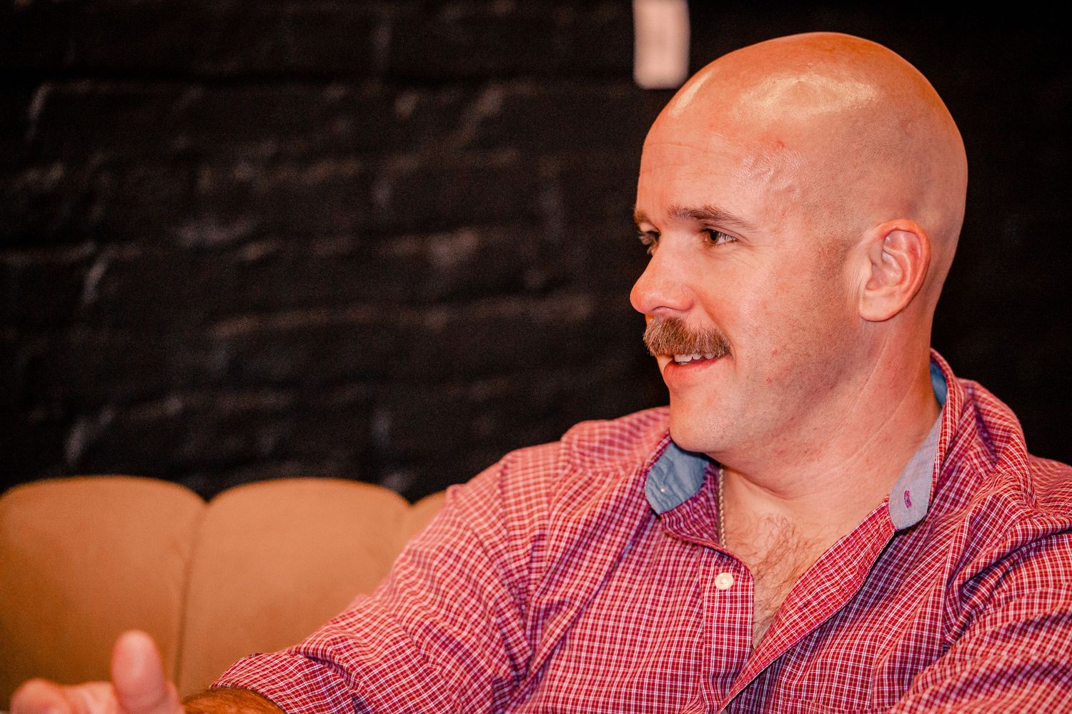 A person in a red checkered shirt smiles during a social event.