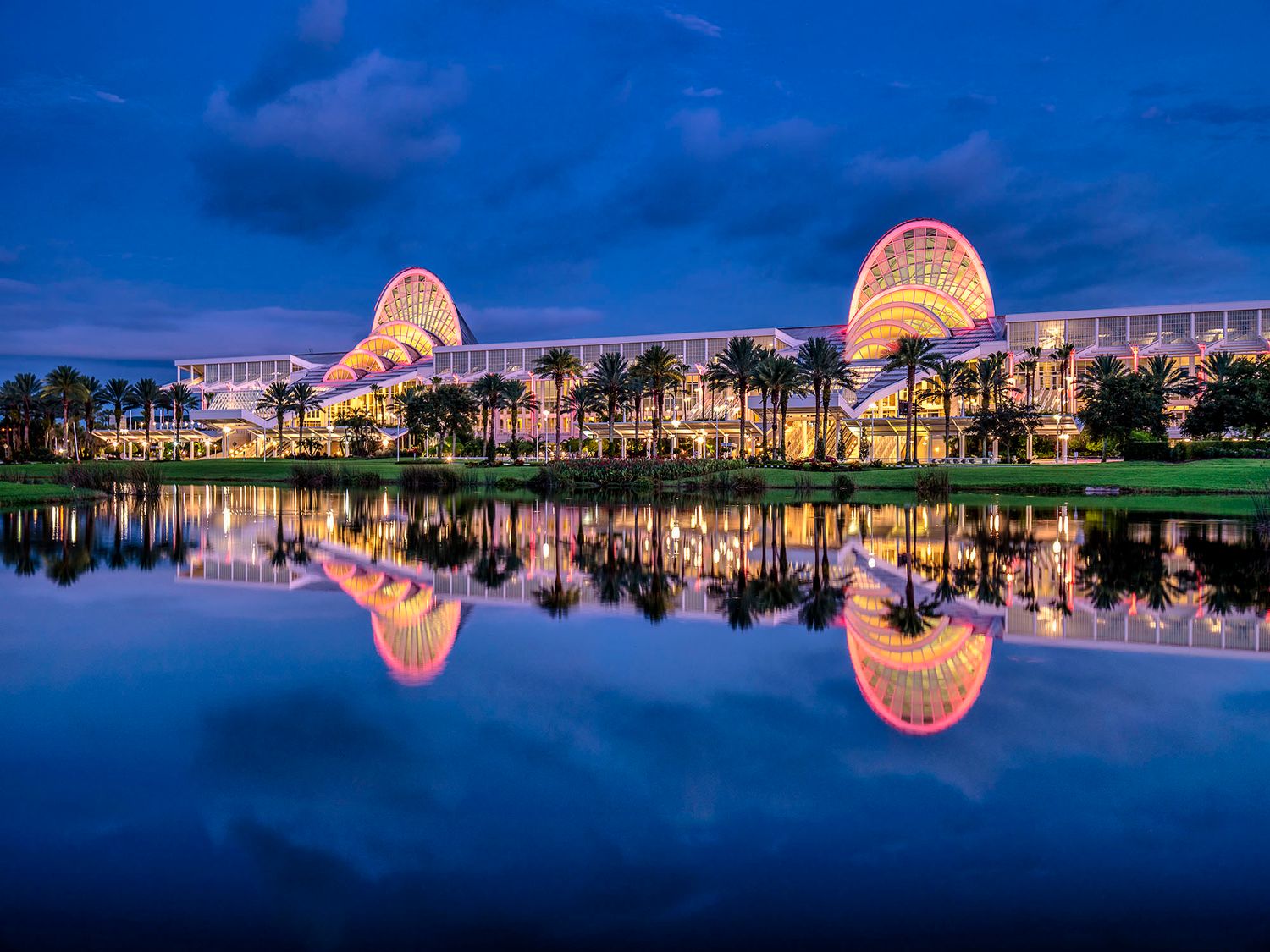 A panoramic sequence of Disney's Beach Club Resort reflecting in Crescent Lake at dusk with glowing orange lights.
