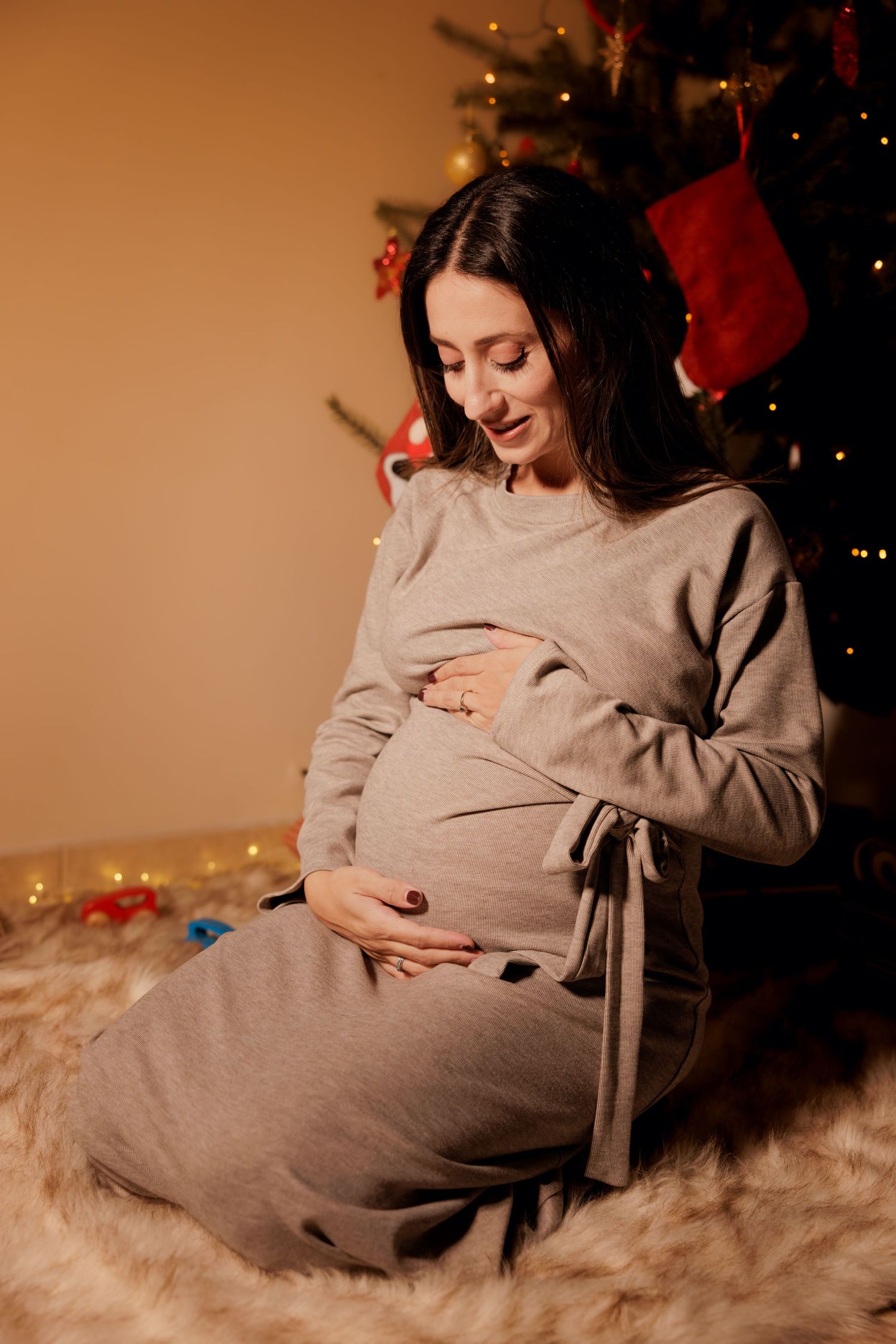 Pregnant woman sitting in warm Christmas lights during a cozy maternity photoshoot in Cyprus
