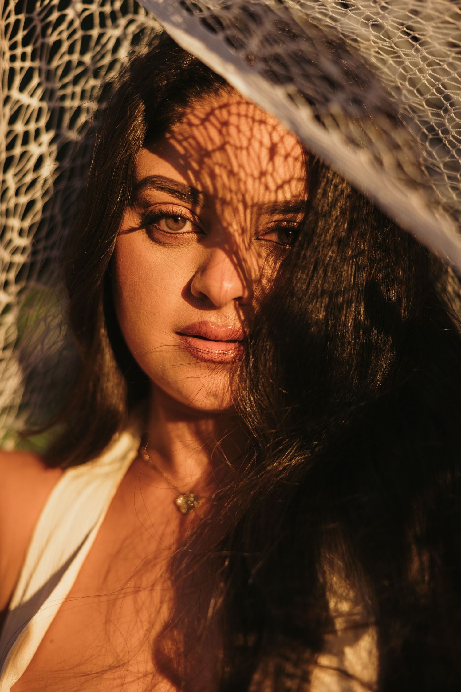 Woman with curly hair posing in warm sunlight with leaf shadows on her face during a Cyprus outdoor photoshoot