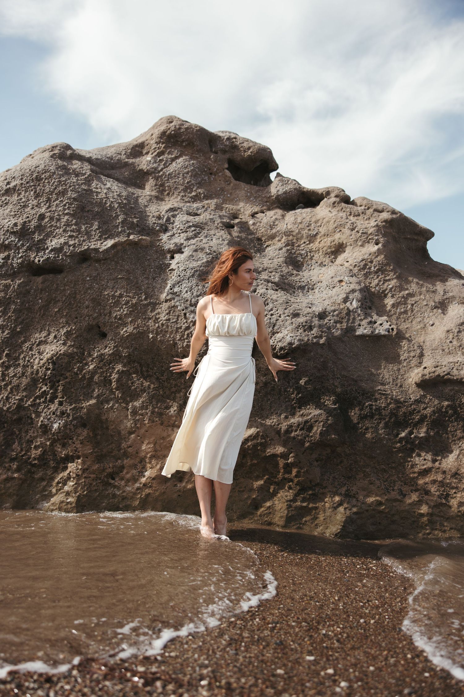 Woman in a white dress standing on coastal rocks during a seaside photoshoot in Cyprus