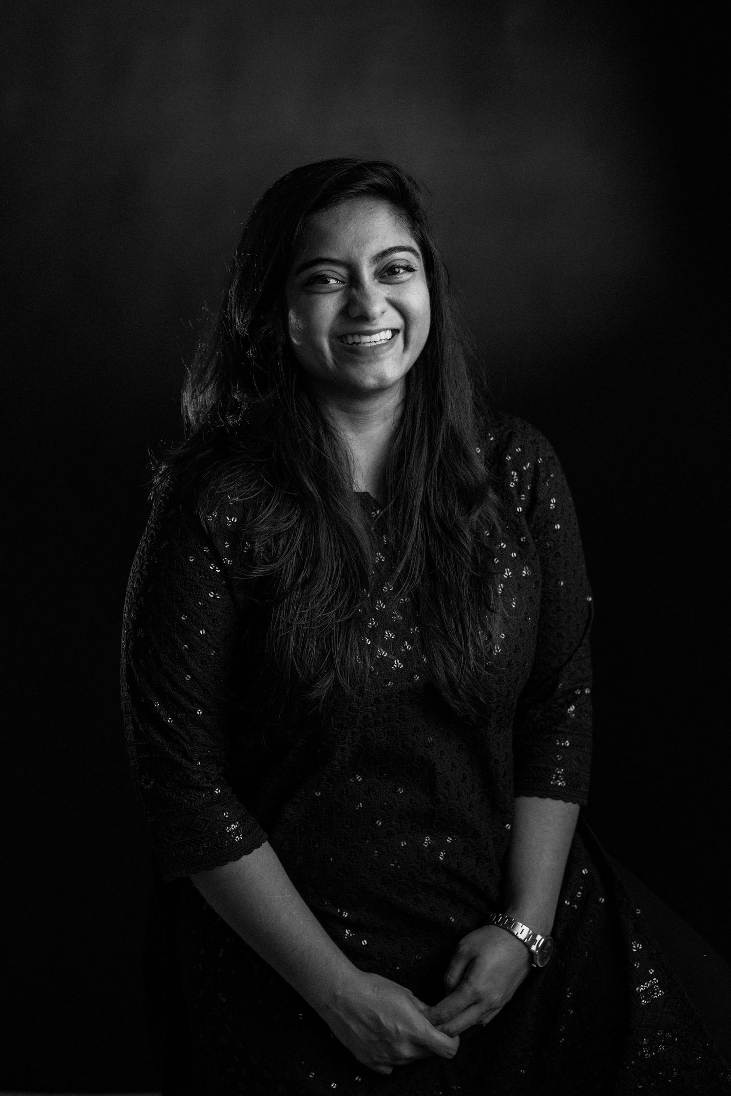 Black and white portrait of someone wearing a sparkly dark traditional dress while smiling warmly at the camera.