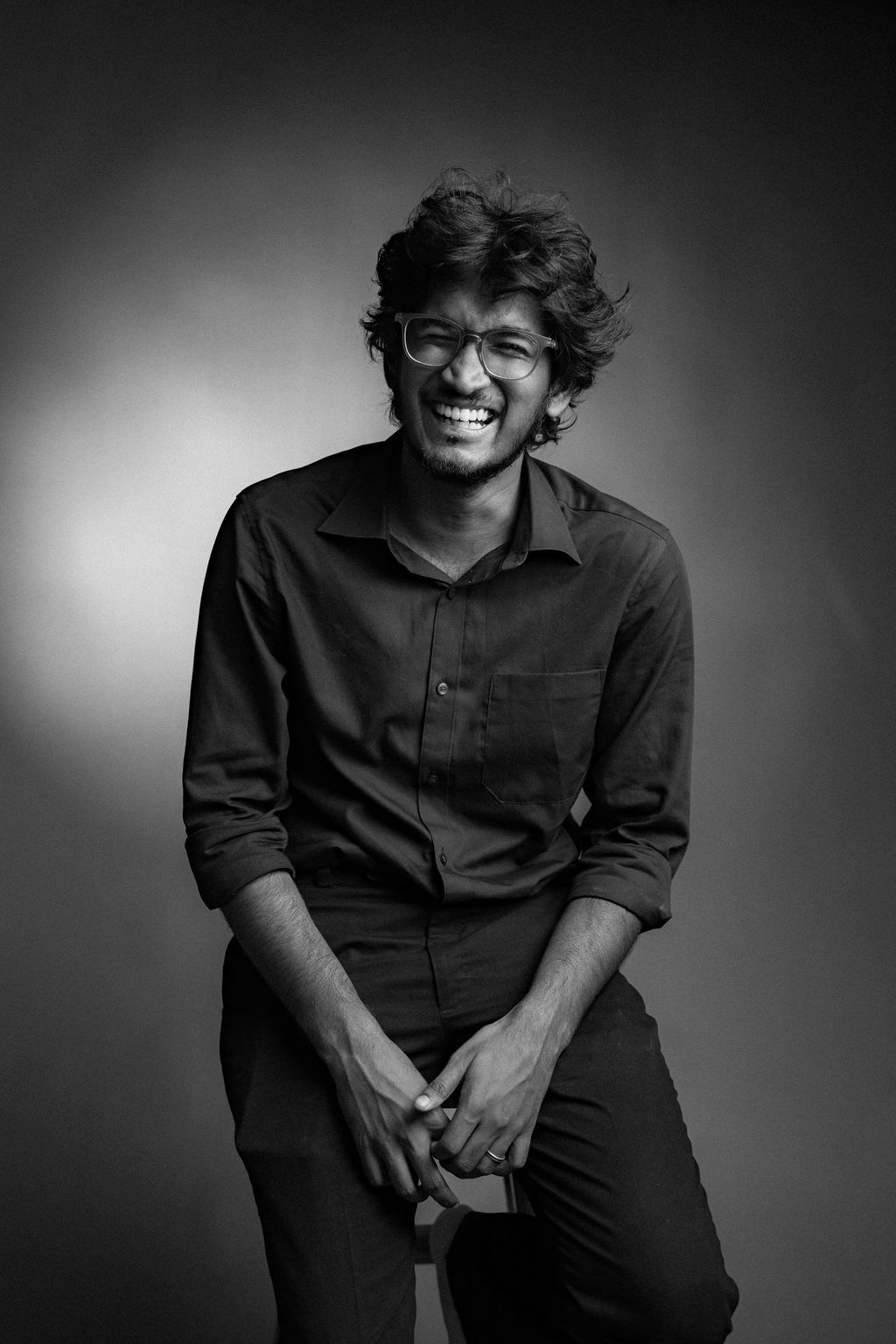 Black and white portrait of a smiling young man with glasses and curly hair wearing a dark shirt.