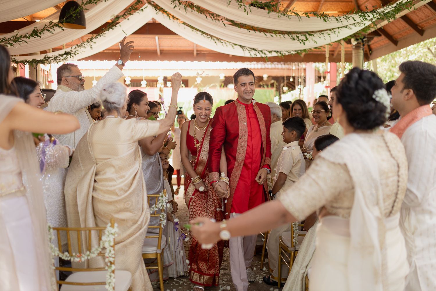 Festive wedding celebration with guests in white attire dancing under a decorated tent canopy.
