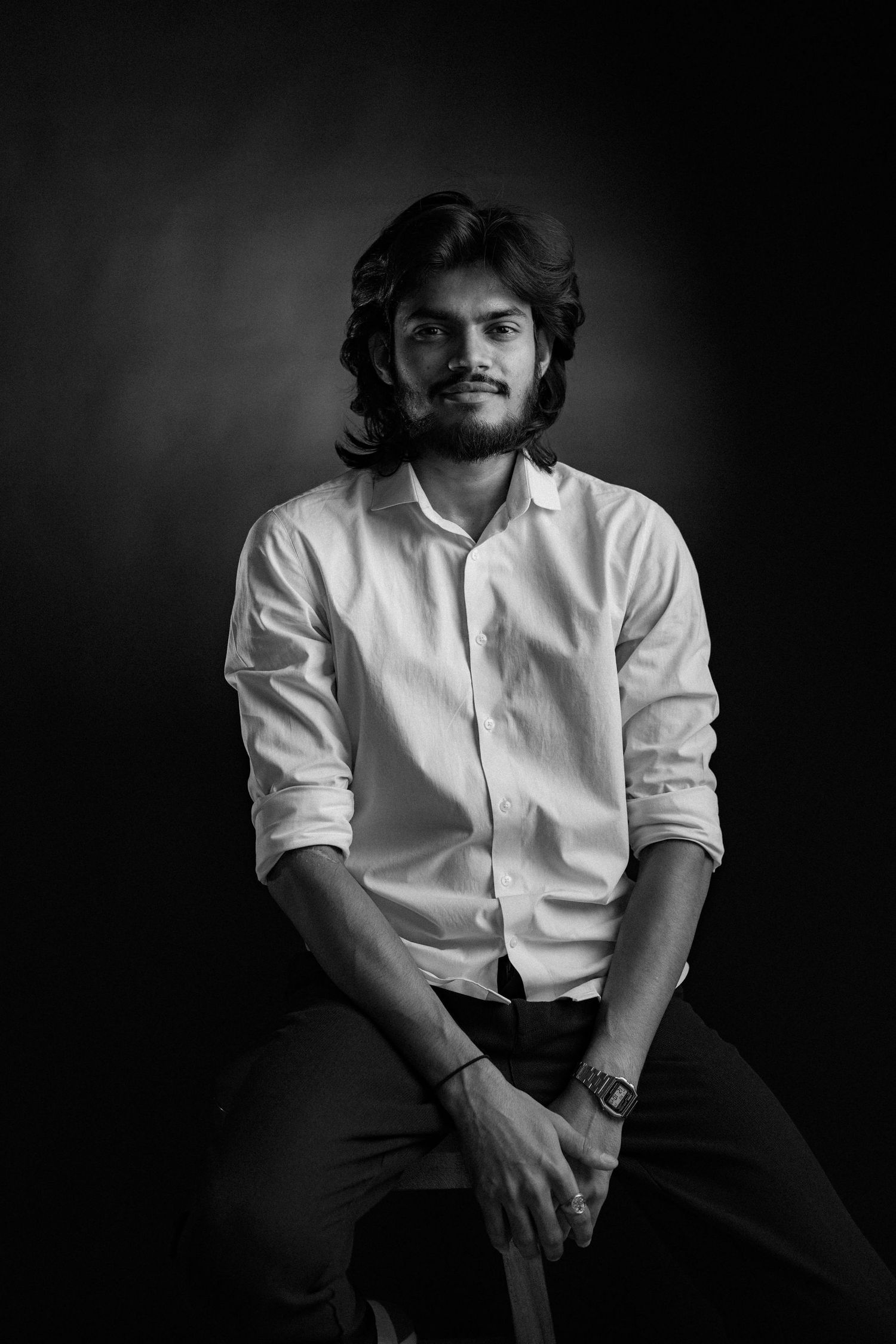 Black and white studio portrait of person in white button-down shirt sitting against dark background.