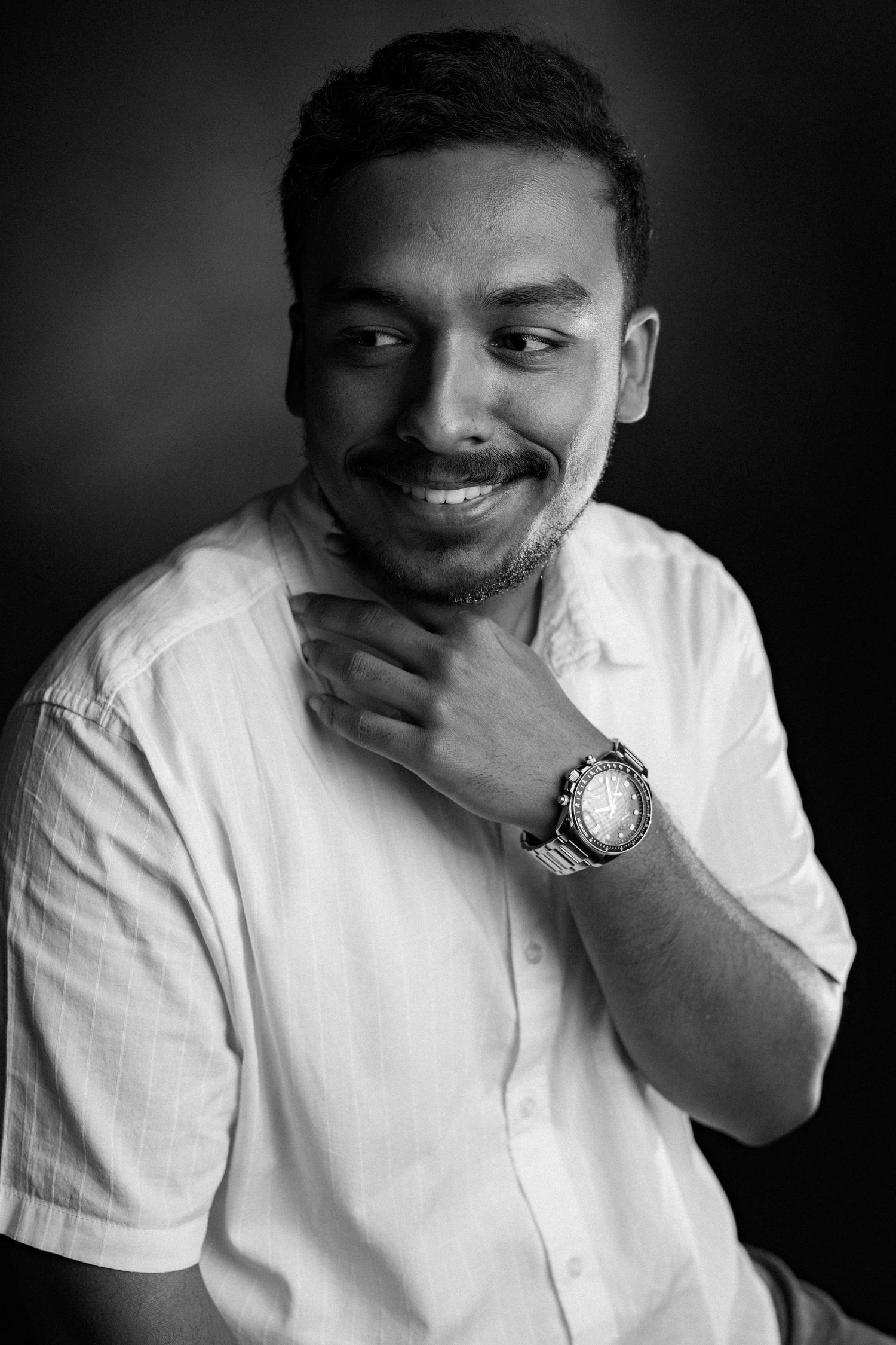Black and white portrait of a person in a white shirt with a warm smile, wearing a wrist watch.